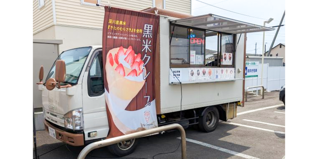 白い車体に「黒米クレープ」ののぼりを掲げ、販売窓にメニューを表示したクレープハウスMAXのキッチンカー。